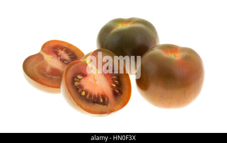 Eine braune Tomate, die in der Mitte neben zwei ganzen Früchten isoliert auf einem weißen Hintergrund in Scheiben geschnitten. Stockfoto