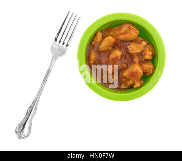 Draufsicht auf eine kleine grüne Schüssel gefüllt mit Brocken Huhn in einer dicken Barbecue-Sauce und eine Gabel zur Seite isoliert auf einem weißen Hintergrund. Stockfoto