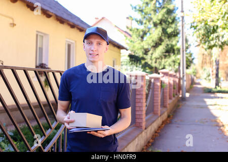 Junge Kurier europäischen aussehen wie Job-Carry-Paket. Mann im schwarzen T-Shirt und Mütze trägt Welcome Box für Kunden, Lieferung Mann Arbeit mit Vergnügen Stockfoto