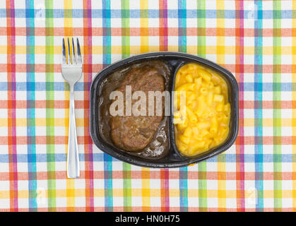 Draufsicht auf ein TV-Diner Essen von Salisbury Steak mit Gravy Makkaroni und Käse in einer schwarzen Schale mit einer Gabel auf die Seite auf einem bunten Tischset. Stockfoto