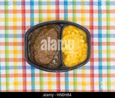 Draufsicht auf ein TV-Diner Essen von Salisbury Steak mit Gravy Makkaroni und Käse in einer schwarzen Schale auf einem bunten Tischset. Stockfoto