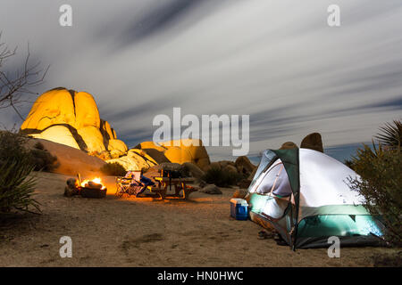 Ein Zelt sitzt ein Lagerfeuer in der Nacht auf einem Campingplatz in Joshua Tree National Park. Stockfoto