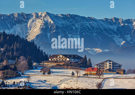 Sonnigen Winterlandschaft mit majestätischen schneebedeckten Piatra Craiului Bergen, Chalet oder Unterkunft Gebäude in Cheile Gradistei Fundata touristische Resort, Rumänien. Stockfoto