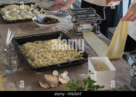 Person, die einer Nudelmaschine mit frisch zubereiteten Pasta und andere Lebensmittel auf Tisch Stockfoto