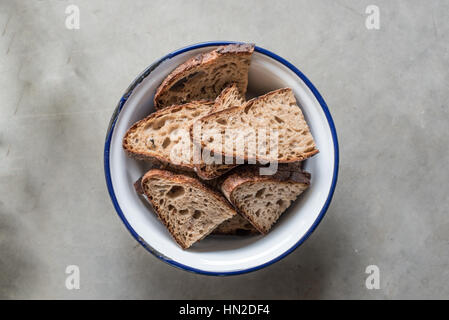 Scheiben von frisch gebackenem Sauerteigbrot in einer weißen und blauen Schüssel auf einem Sichtbeton-Hintergrund Stockfoto