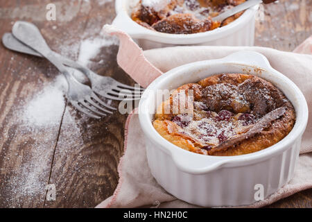 Hausgemachte traditionelle französische Dessert Kirsch Clafoutis in Keramik Förmchen auf rustikalen Tisch Stockfoto