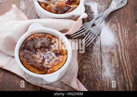 Hausgemachte traditionelle französische Dessert Kirsch Clafoutis in Keramik Förmchen auf rustikalen Tisch Stockfoto