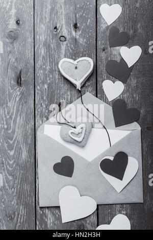 Umschlag mit handgeschöpftem Papierherzen und Form Herzkekse auf rustikalen Holztisch blau. Valentinstag-Grußkarte mit schwarzen & weißen Sepia-Effekt, Stockfoto