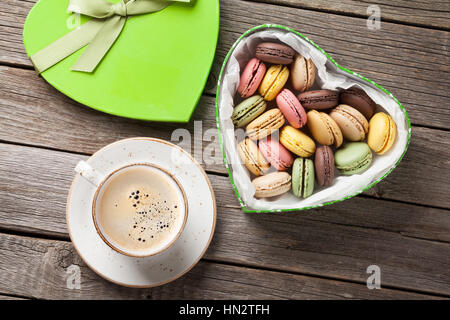 Bunte Macarons in Valentinstag herzförmigen Geschenk-Box und Kaffee Tasse auf Holztisch. Ansicht von oben Stockfoto