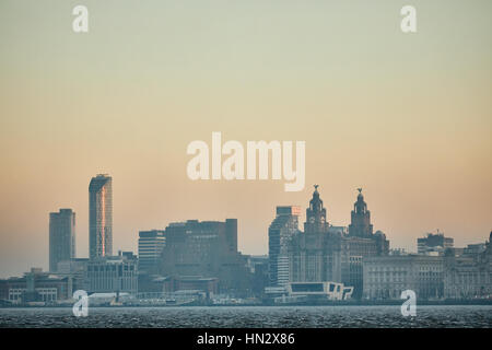 Von Birkenhead Seite den Fluss Mersey, Blick auf den orangefarbenen Himmel Sonnenaufgang über Liverpool City Centre Wahrzeichen Waterfront Skyline in Merseyside, Stockfoto