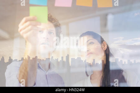 Unternehmer und Unternehmerin kleben Klebefuge Notizen auf Glaswand im Büro Stockfoto