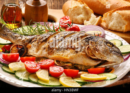 Gegrillter Fisch mit Baguette und Gemüse auf dem Teller Stockfoto