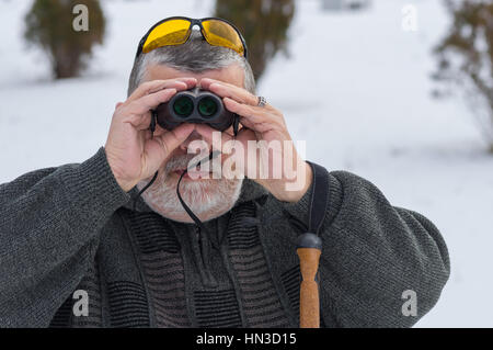Outdoor Portrait kaukasischen senior bärtigen Blick durch ein Fernglas auf Wintersaison Stockfoto