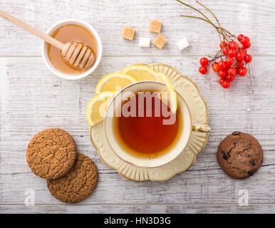 Tee mit Zitrone. Cookies, Zucker, Honig und Viburnum auf einem weißen Holztisch liegen. Stockfoto