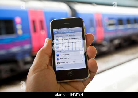 Bristol, Vereinigtes Königreich - 4. Oktober 2011: eine männliche Hand hält ein Apple iPhone 3Gs an Bristol Temple Meads Station mit Eisenbahnwaggons aus focu Stockfoto