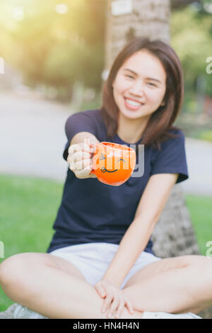 glücklich trinken Kaffee-Konzept mit Textfreiraum, asiatisches Mädchen Teen arbeiten Frauen adult Griff Lächeln Becher in den grünen Park. Stockfoto