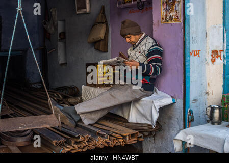 Indischen Mann liest eine Newsapaper in seiner Werkstatt Metall Träger, Agra Stockfoto