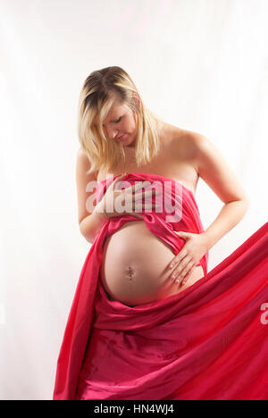 Schöne blonde behaarte schwangere junge Frau in Rosa Seide wickeln Stockfoto