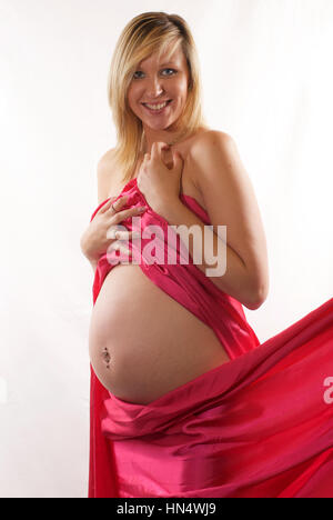Schöne blonde behaarte schwangere junge Frau in Rosa Seide wickeln Stockfoto