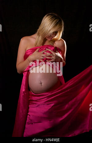 Schöne blonde behaarte schwangere junge Frau in Rosa Seide wickeln Stockfoto