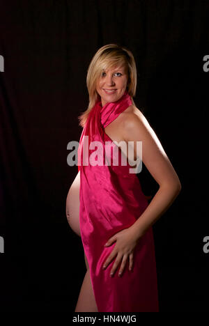 Schöne blonde behaarte schwangere junge Frau in Rosa Seide wickeln Stockfoto
