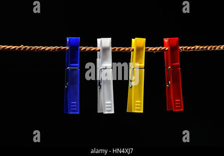 Vier farbige Wäscheklammern hängen in einer Reihe auf schwarzem Hintergrund Stockfoto