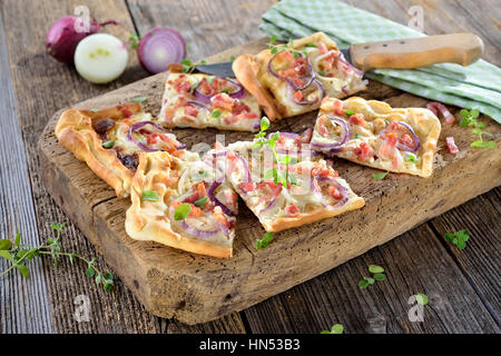 Heiße gebackene Flammkuchen Flammkuchen aus dem Elsass mit Zwiebeln, Speck und Sauerrahm serviert auf einem schäbigen Holzbrett Stockfoto