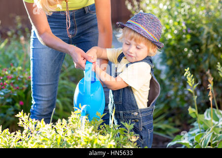 Kind mit Mama im Garten arbeiten. Kind Bewässerung Blumen. Mutter hilft kleinen Sohn. Stockfoto