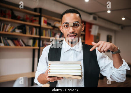 Bild der schönen afrikanischen Jungunternehmer tragen Brillen in Bibliothek halten Notebooks stehen. Schauen Sie sich die Kamera und zeigen. Stockfoto