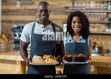 Porträt von Kellner und Kellnerin, die Halteplatte der Cupcake und Croissant am Schalter im CafÃƒÂ © Stockfoto