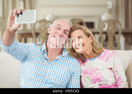 Älteres Paar, wobei ein Selbstporträt auf Handy im Wohnzimmer zu Hause Stockfoto