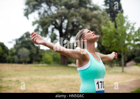 Sportlerin mit Armen ausgestreckt im Park am sonnigen Tag Stockfoto