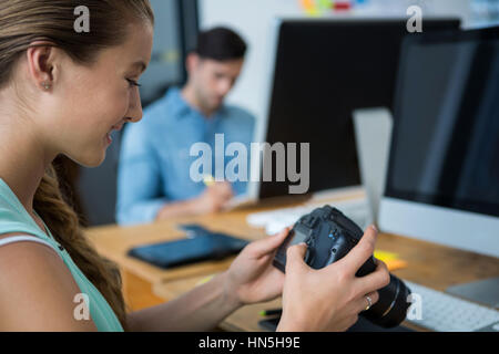 Weibliche Grafiker überprüfen aufgenommenen Bilder in seiner Digitalkamera am Schreibtisch im Büro Stockfoto