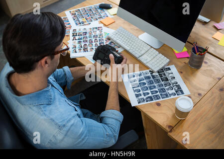 Mann am Schreibtisch hält Digitalkamera im Büro Stockfoto