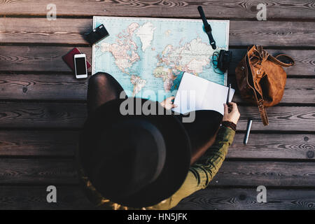 Draufsicht der Frau Hut machen Tour-Plan mit einer Weltkarte. Touristische Erkundung der Welt Karte mit Reise-Accessoires rund um. Stockfoto