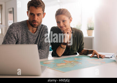 Junger Mann und Frau betrachten Laptop-Computer mit Weltkarte vor. Paar mit Technologie, um die Welt zu erkunden. Stockfoto