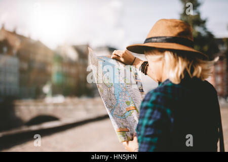 Seitenansicht der jungen Frau mit Hut, Blick auf einen Stadtplan. Touristen auf der Suche nach Navigationsroute auf Karte. Stockfoto