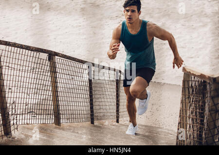 Fitness-Mann läuft die Treppe hinauf am Strand. Muskulösen jungen männlichen Läufer arbeiten auf Schritte am Meeresufer. Stockfoto