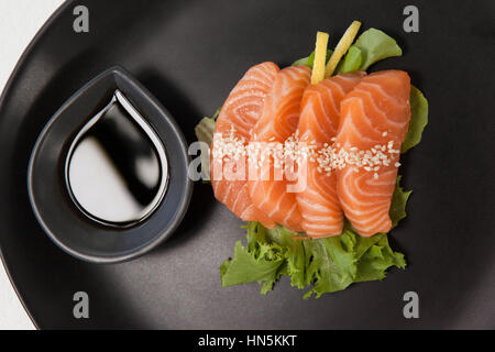 Nahaufnahme von vier Sashimi Sushi mit Sojasauce in schwarze Platte serviert Stockfoto