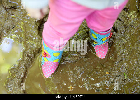 Ein junges Mädchen tragen ihre Gummistiefel und stehende Knöchel tief in nassen ein dicken schlammigen Pfütze Stockfoto