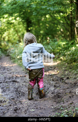 Ein junges Kind Hols der Rückseite der Hose Weg von ihrem Körper nach einem Sturz auf den Hintern im nassen Schlamm Stockfoto