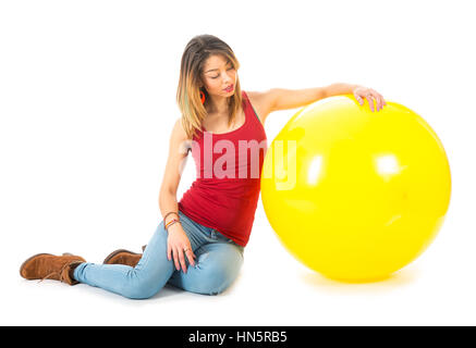 Schöne Frau mit rotem Hemd auf Boden sitzend, mit einem großen gelben Ballon isoliert auf weißem Hintergrund Stockfoto