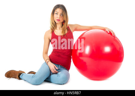 Schöne Frau mit rotem Hemd auf Boden sitzend, mit einem großen roten Ballon isoliert auf weißem Hintergrund Stockfoto