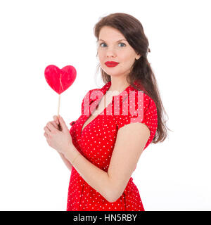 Schöne Frau im roten Kleid mit roten herzförmigen Lutscher vor ihr isoliert auf weiss Stockfoto