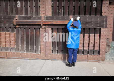 Kyoto, Japan - 19. März 2012: Ein Wachmann in eine blaue uniform sperrt das große hölzerne Eingangstor zum Nijo Burg in Kyoto, Japan. Stockfoto