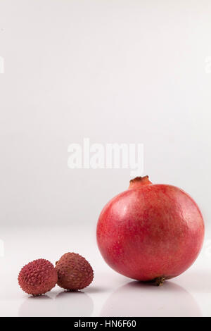 Vertikale Aufnahme von Granatapfel und zwei Litschis auf einem weißen Backgroung platziert Stockfoto