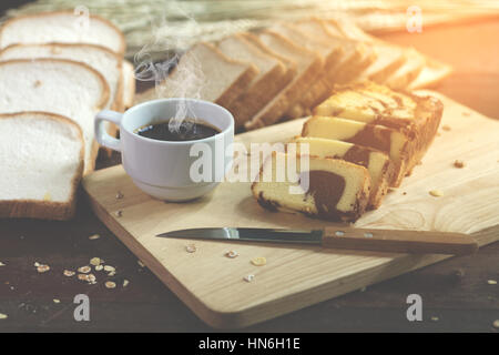 Butter Kuchen in Scheiben geschnitten und heißen Kaffee am Holztisch. weiche Flare Sonnenlicht. Stockfoto