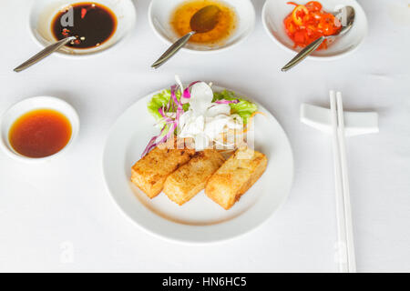 Dim Sum essen gebratene Rübe Kuchen in weißer Teller im Restaurant mit Sojasauce, süße Sauce, Chili-Sauce und Stäbchen. Stockfoto