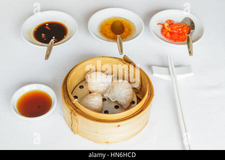 Dim Sum Essen dampfgegarte Garnelen Har Gow Knödel im Bambuskorb im Restaurant mit Sojasauce, süße Sauce, Chili-Sauce und Stäbchen. Stockfoto