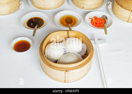 Dim Sum Essen dampfgegarte Sahne Pudding Brötchen im Bambuskorb im Restaurant mit Sojasauce, süße Sauce, Chili-Sauce und Stäbchen. Stockfoto